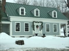 a blue house with wreaths on the front door and windows in the snow covered yard