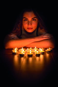 a woman sitting in front of candles with her arms folded over her head and looking at the camera