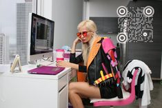 a woman sitting at a desk in front of a computer and holding a pink cup