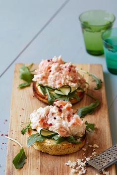 two open faced sandwiches with cucumbers and herbs on a cutting board next to glasses