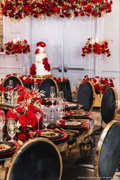 the table is set with black and gold plates, silverware, red flowers and candles