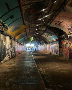 an empty tunnel with graffiti all over the walls and floor, along with people walking down it