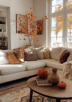 a living room filled with white furniture and lots of fall decorations on the coffee table