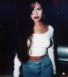 a woman standing in front of a car wearing high waist jeans and a crop top