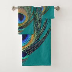 two towels hanging on a towel rack in front of a white wall with peacock feathers