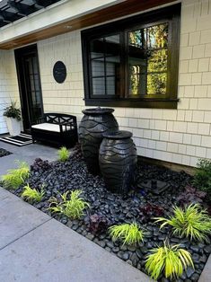 two large vases sitting on top of a black rock bed in front of a house