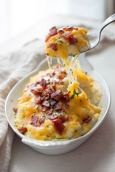 a white bowl filled with mashed potatoes covered in bacon and cheese, being held by a fork