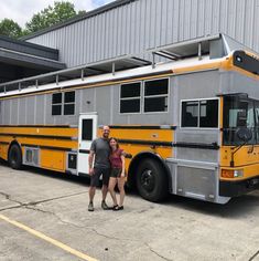 two people standing in front of a yellow and gray bus