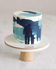 there is a small cake with a man and dog on the top, sitting on a stand