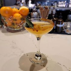 a glass filled with liquid sitting on top of a table next to some oranges