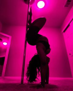 a woman is doing a handstand on a pole in a room with pink lights