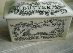 a white butter jar with a bow on top sitting on a cloth covered tablecloth