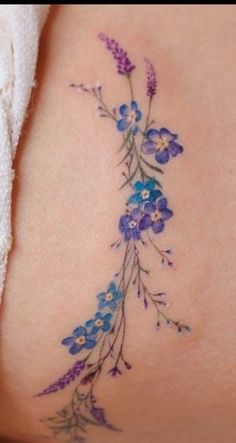 a woman's back tattoo with blue flowers on the side and purple petals at the bottom