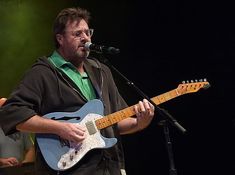 a man standing in front of a microphone while holding a guitar