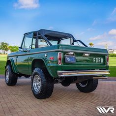 a green truck parked on top of a brick road