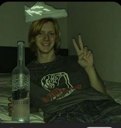 a person sitting on a bed with a bottle and peace sign in front of them