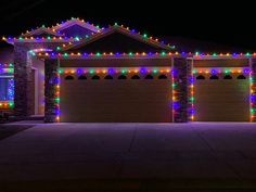 a house with christmas lights on the roof and garage doors in front of it at night