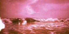 an image of the ocean with waves coming in to shore and pink hued sky