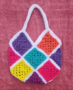 a multicolored crocheted bag sitting on top of a pink blanket