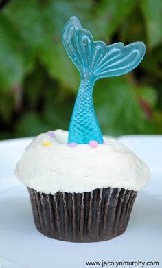 a cupcake with white frosting and a blue mermaid tail on top is sitting on a plate