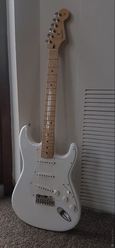 a white electric guitar sitting on the floor in front of a wall with a radiator