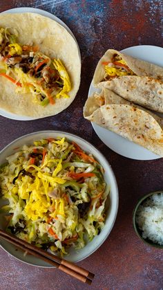 two burritos with shredded vegetables and rice in bowls next to chopsticks