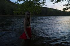 a woman in a red dress standing in the middle of a body of water at sunset