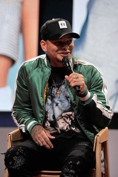 a man sitting in a chair while holding a microphone to his mouth and wearing a hat