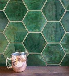 a metal cup sitting on top of a wooden table next to a green tiled wall