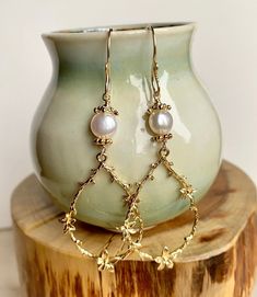 Enhance your boho chic style with this set of long gold teardrop-shaped flower branch dangly earrings. Featuring large gold-plated brass flower branch charms, these earrings are delicately crafted and exude a sweet charm. The handmade earring hooks, crafted with 10K gold-filled wire, add a touch of elegance. At the top, white freshwater pearls with gold-plated floral bead caps provide a classic and timeless accent. Measuring 2 1/2" X 7/8", including the gold-filled wire hooks, these earrings are Gold Feminine Dangle Flower Earrings, Whimsical Gold Flower Earrings, Gold Flower Chandelier Earrings Elegant Style, Delicate Gold Chandelier Earrings With Pearl Drop, Elegant Brass Earrings With Dangling Charms, Gold Flower-shaped Elegant Chandelier Earrings, Elegant Gold Flower Chandelier Earrings, Feminine Gold Dangle Pearl Earrings, Bohemian Teardrop Pearl Earrings With Ear Wire