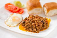 a plate with eggs, meat and vegetables on it next to some bread rolls in the background