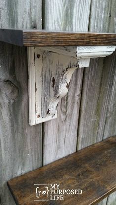 an old wooden shelf is attached to the side of a wall with a rusted metal hook