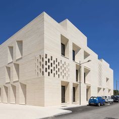 the building is made out of blocks and has many windows on each side, along with cars parked in front of it