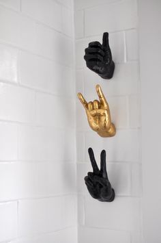 three black and gold hand sculptures hanging on the side of a white tiled bathroom wall