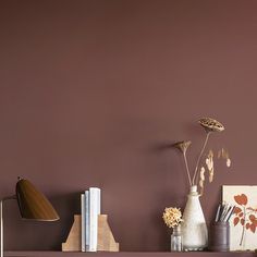 a shelf with vases, books and other items on it in front of a purple wall