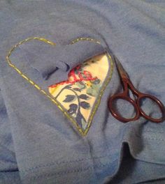 a pair of scissors sitting on top of a blue shirt with a heart shaped pocket