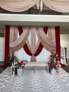 a stage set up for a wedding with red drapes and flowers on the floor