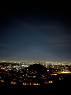 the city lights shine brightly in the dark night sky as seen from atop a hill