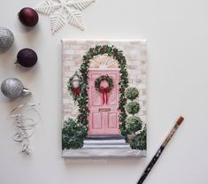 a christmas card with a pink door and wreath on it, surrounded by other holiday decorations