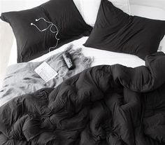 an unmade bed with black sheets and pillows on top of it, next to a remote control