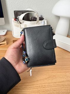 a hand holding a black leather wallet on top of a wooden table next to a computer