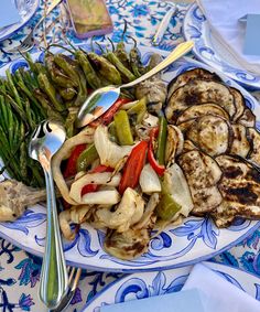 a plate full of grilled vegetables on a blue and white table cloth with utensils