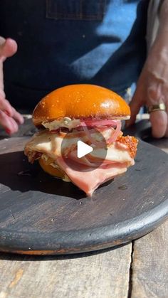 a ham and cheese sandwich sitting on top of a wooden table next to someone's hand