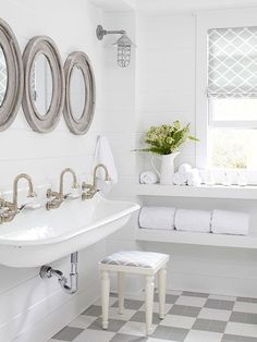 a white bathroom with three mirrors above the sink and two stools in front of it