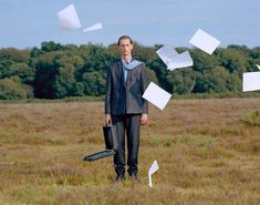 a man in a suit and tie standing in a field with papers flying around him