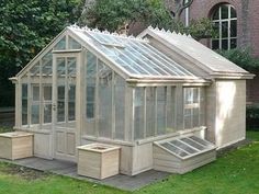 a small wooden greenhouse in the middle of a grassy area next to a brick building