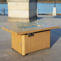 a wooden table sitting on top of a cement ground next to a body of water