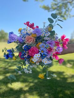 a person holding a bouquet of flowers in their hand on the grass with trees in the background