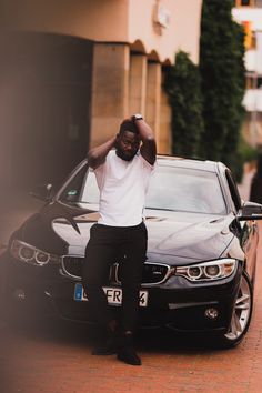 a man sitting on the hood of a black car with his hands behind his head