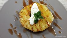 a piece of pineapple with whipped cream and mint leaves on it, sitting on a gray plate